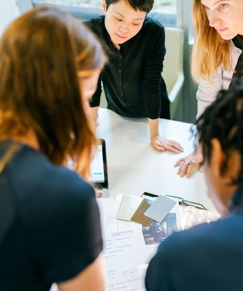 Gruppe von Personen arbeitet gemeinsam an einem Tisch und bespricht Unterlagen in einem hellen Büro.