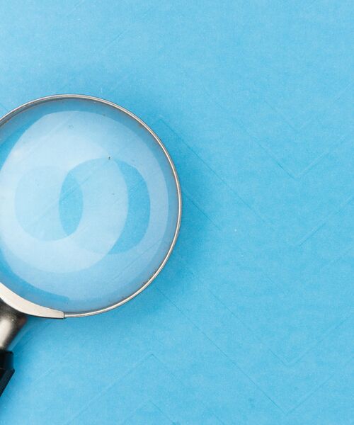 Lupe auf hellblauem Hintergrund, die eine vergrößerte Fläche im Glas zeigt.