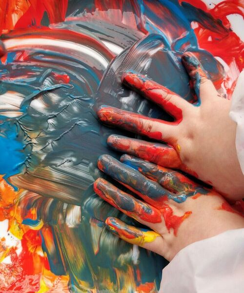 Kinderhände verstreichen bunte Fingerfarben auf einer weißen Fläche.