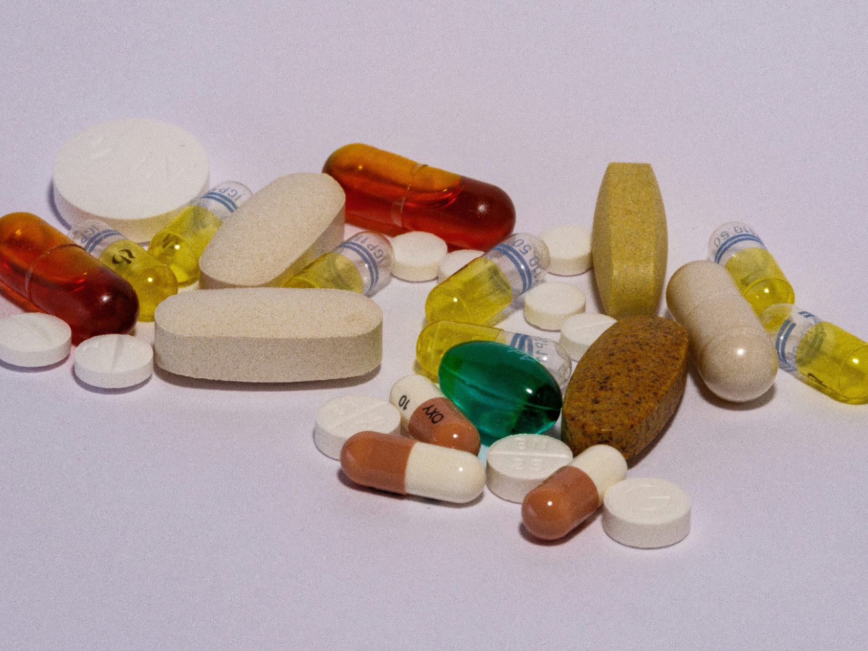 Verschiedene Tabletten und Kapseln in unterschiedlichen Farben und Formen liegen auf einer hellen Oberfläche.