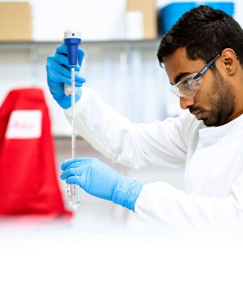 Person im Labor führt mit Schutzbrille und Handschuhen eine Pipettierarbeit durch.