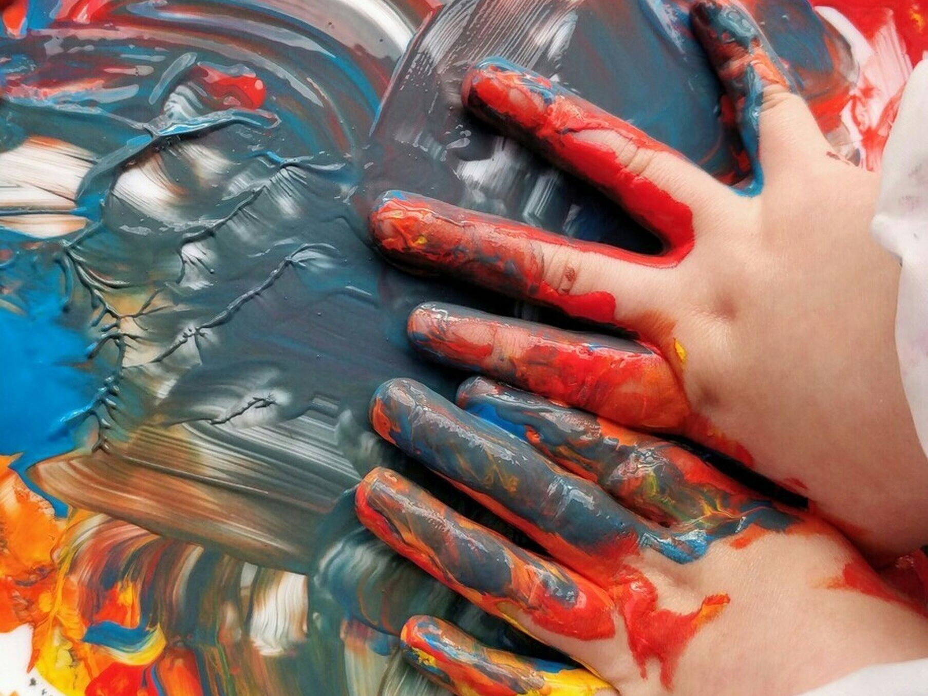 Kinderhände verstreichen bunte Fingerfarben auf einer weißen Fläche.