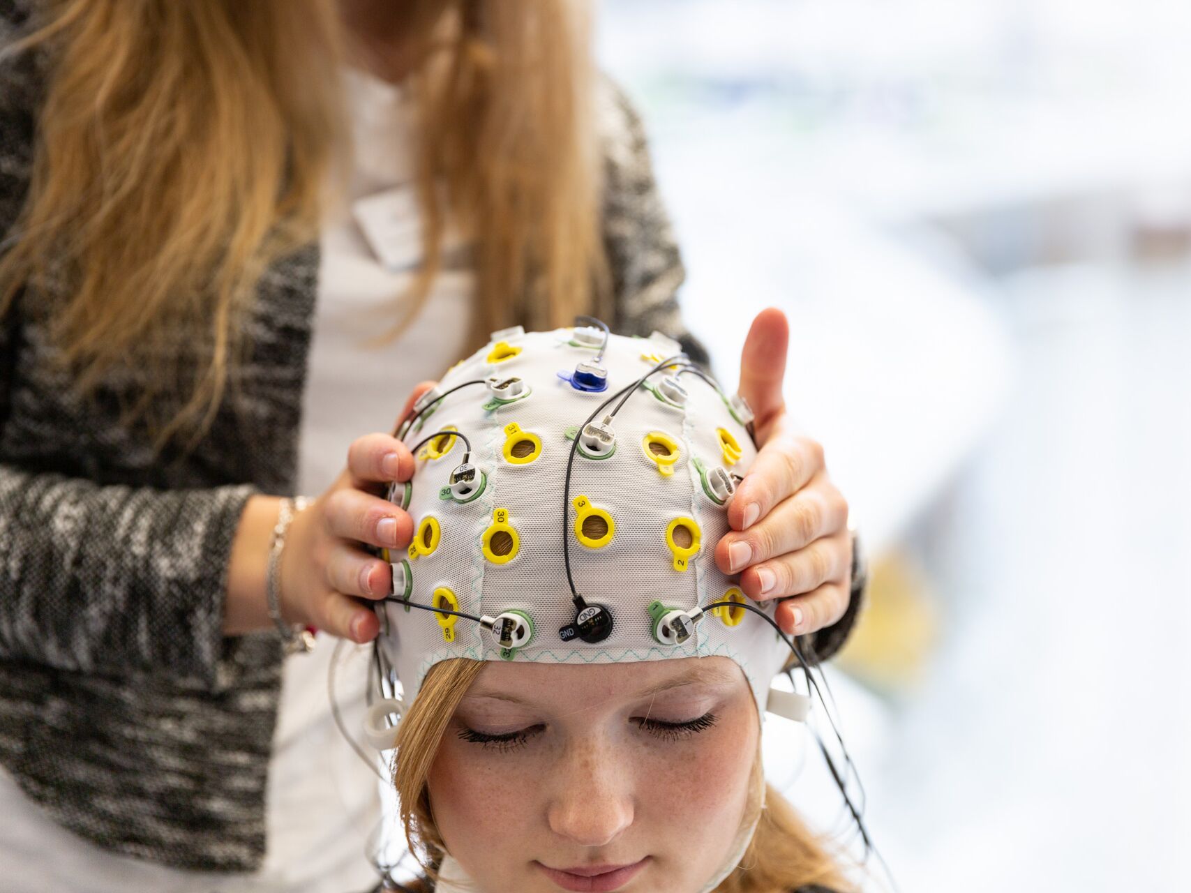Person trägt eine EEG-Messhaube mit Elektroden, eine zweite Person justiert sie behutsam.