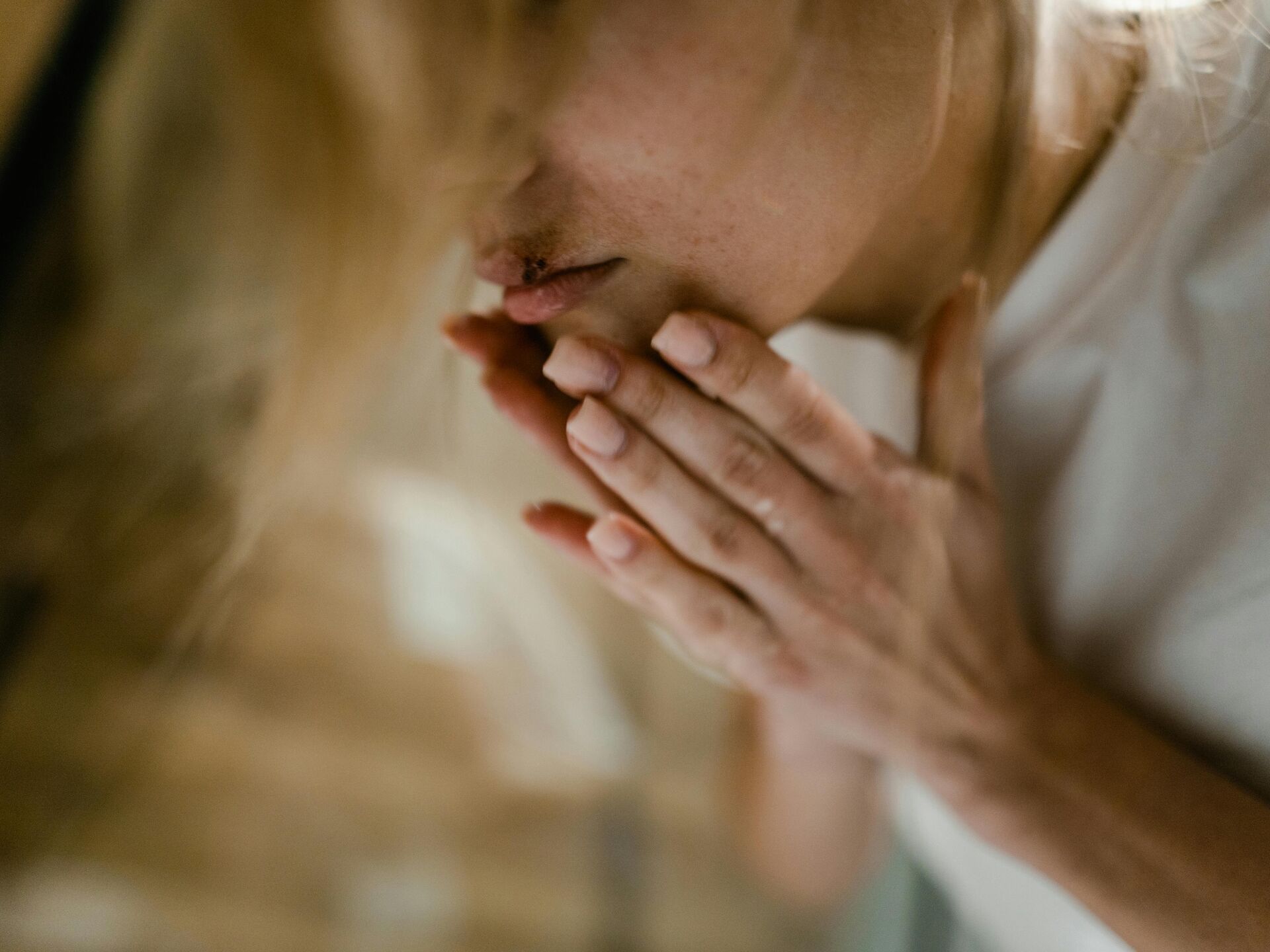 Person hält sich mit beiden Händen den Mund, Nahaufnahme des Gesichts mit neutralem Hintergrund.